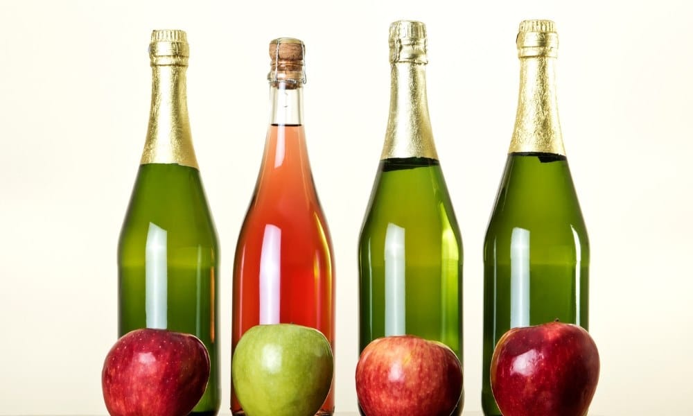 Quatre bouteilles remplies de cidre avec des pommes